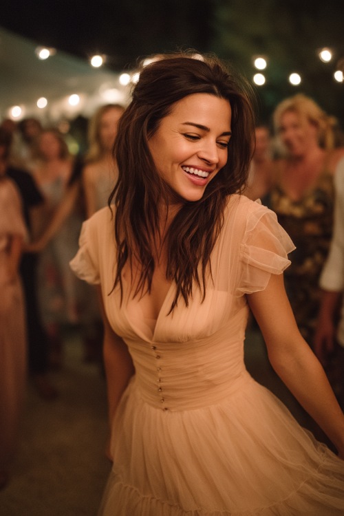 A woman wearing a tulle layered blush dress with a flowy silhouette and short sleeves, dancing beside a wedding reception under string lights