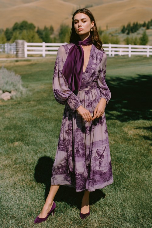 A woman wears a deep lavender ombré chiffon gown printed with a tonal pastoral toile pattern, featuring billowing poet sleeves gathered at the cuff