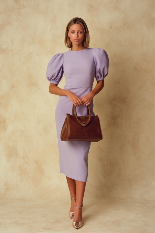 Classy woman in a soft lavender puff-sleeve midi dress, holding a structured leather handbag, standing elegantly in a studio with a pale cream backdrop 