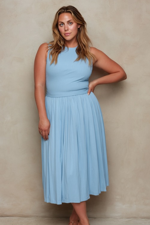 Elegant plus-size woman wearing a soft sky blue sleeveless midi dress with subtle pleats and slip-on sandals, standing confidently in front of a light taupe studio wall