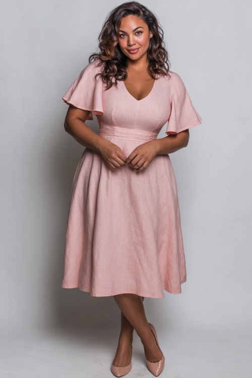 Plus-size woman wearing a soft rose pink linen fit-and-flare midi dress with flutter sleeves and classic flats, standing gracefully against a soft white studio wall