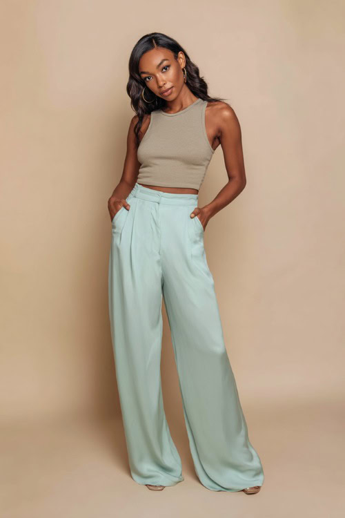 Stylish Black woman in soft mint green silk wide-leg trousers paired with a fitted sleeveless tank, posing confidently in a luxury fashion studio with a matte cream backdrop