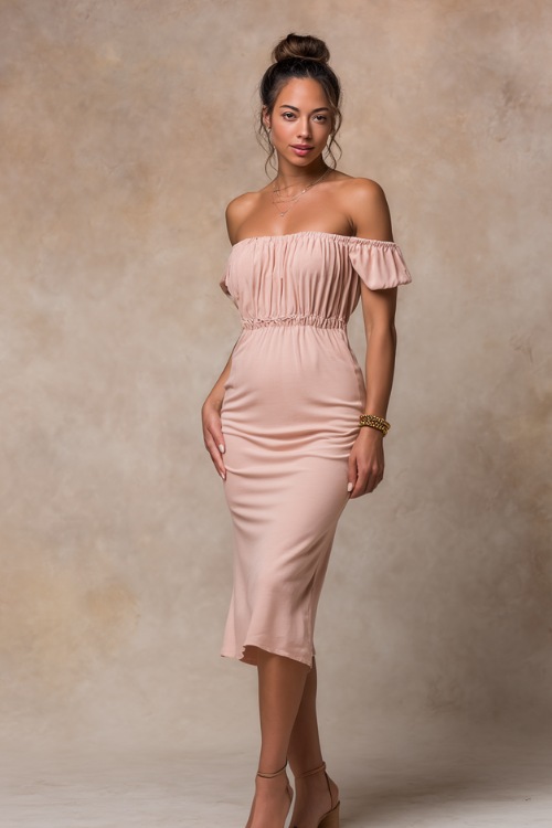 Stylish lady wearing a light blush pink off-the-shoulder midi dress with dainty gold bracelet and strappy sandals, standing confidently against a soft stone-colored studio backdrop 