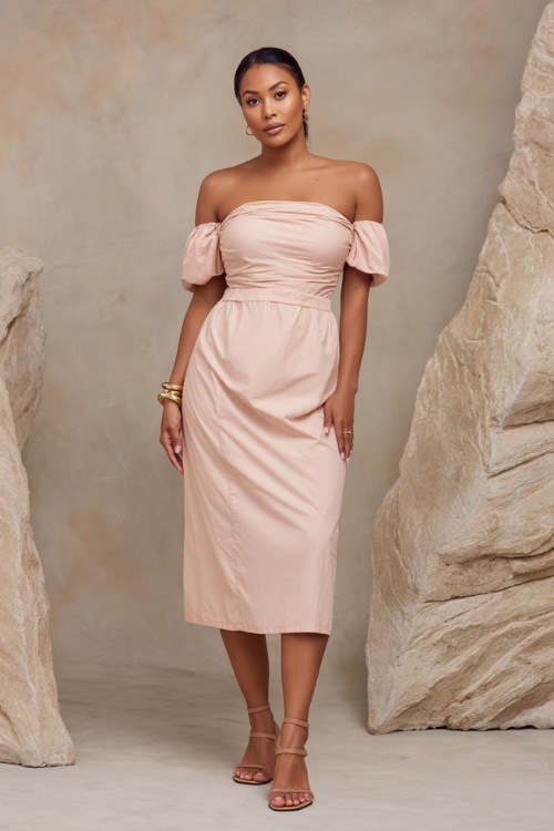 Stylish lady wearing a light blush pink off-the-shoulder midi dress with dainty gold bracelet and strappy sandals, standing confidently against a soft stone-colored studio backdrop