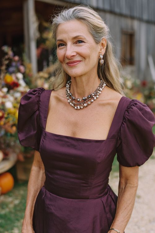 A woman over 50 wears a deep plum midi dress with satin puff sleeves, a square neckline, and a softly gathered skirt