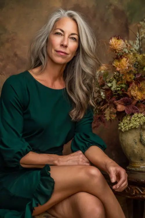 Elegant full body of a woman over 50 wearing a forest green crepe dress with fluted hem and elbow sleeves, surrounded by warm-toned floral decor