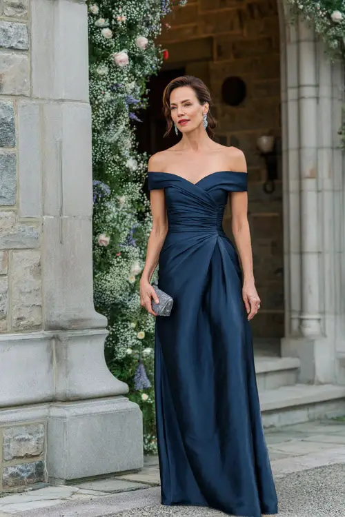 Elegant woman over 50 wearing a floor-length navy blue off-shoulder gown with structured bodice, soft pleats