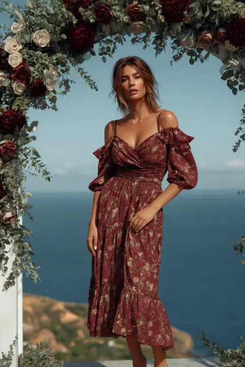 Full body of a mature woman in a wine floral midi dress with ruffled sleeves and tiered skirt, standing beside a fall wedding arch with burgundy roses and eucalyptus