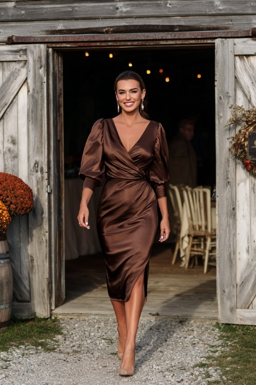 Full body of a woman in a chocolate brown satin midi wrap dress with subtle sheen and puff sleeves, wearing gold earrings and heels 