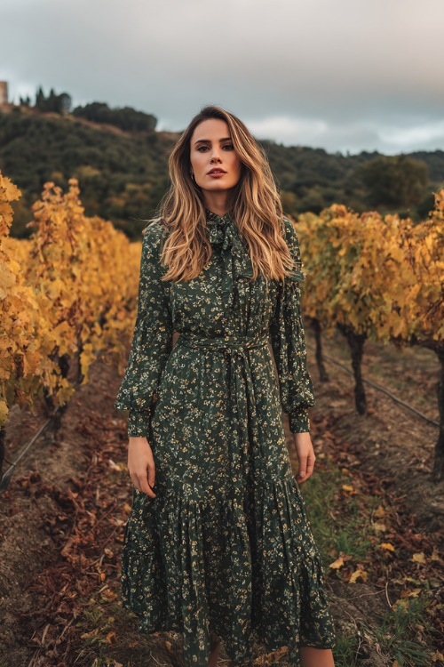 Full body of a woman styled for a smaller frame wearing a forest green floral chiffon midi dress with a ruffled hem and a fitted waist