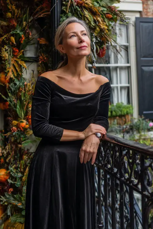 Mature woman in a black velvet gown with bateau neckline and A-line shape, standing beside a wrought iron railing wrapped in autumn garlands