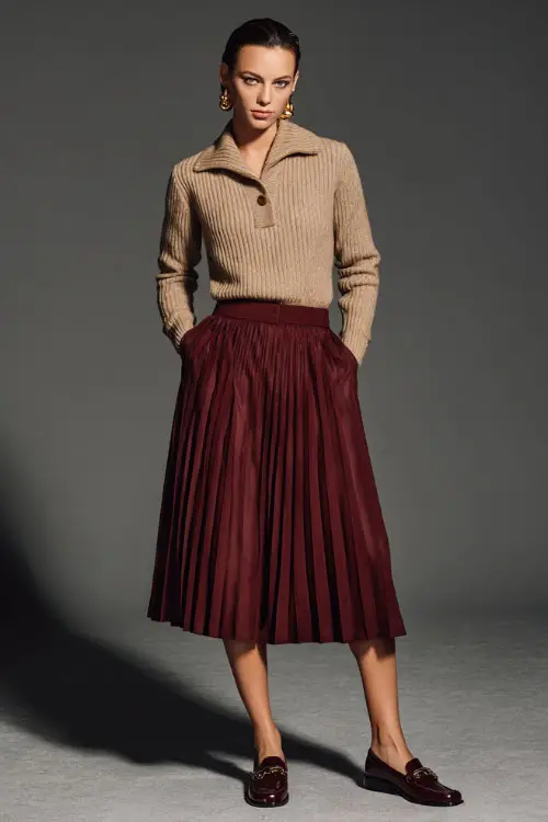 Woman in a burgundy pleated midi skirt and camel knit pullover, styled with vintage earrings and leather loafers, full-body in clean studio setting 