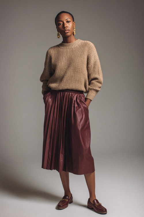 Woman in a burgundy pleated midi skirt and camel knit pullover, styled with vintage earrings and leather loafers, full-body in clean studio setting