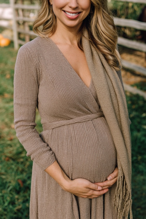 Woman wearing a warm taupe ribbed knit dress with a midi hemline, wrap waist, and soft scarf, styled for comfort during pregnancy at a cozy outdoor October wedding