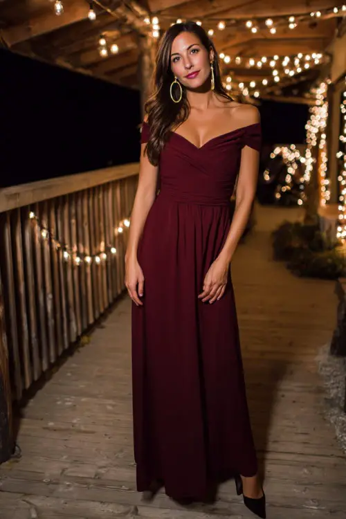 Woman in a deep burgundy floor-length gown with an off-the-shoulder neckline, paired with black heels and gold hoops