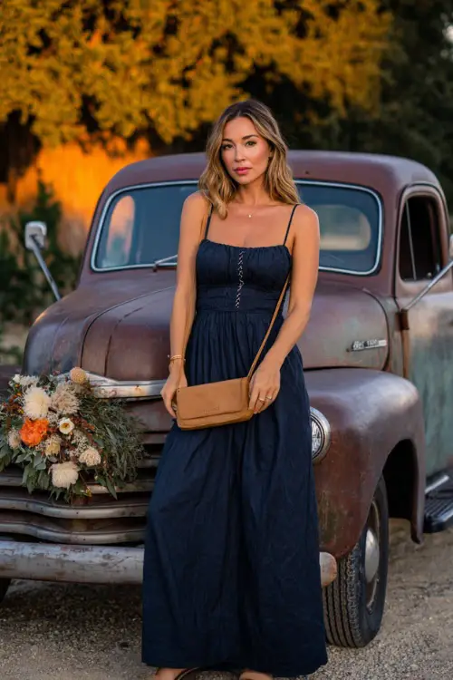 Woman in a navy empire-waist maxi dress with subtle embroidery, styled with a tan crossbody bag and block-heel sandals