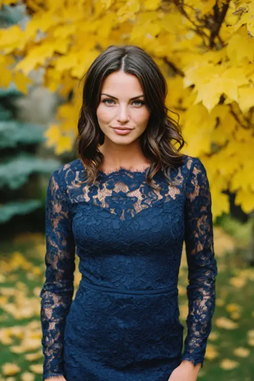 Woman in a navy lace dress with scalloped hem and long sleeves, posing under golden maple trees at a scenic October wedding venue, full body 