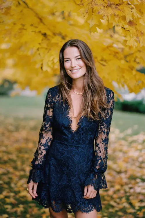 Woman in a navy lace dress with scalloped hem and long sleeves, posing under golden maple trees at a scenic October wedding venue, full body