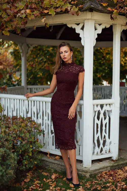 Woman wearing a burgundy lace midi dress with scalloped edges and cap sleeves, accessorized with pearl drop earrings and black heels 