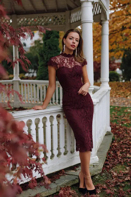 Woman wearing a burgundy lace midi dress with scalloped edges and cap sleeves, accessorized with pearl drop earrings and black heels