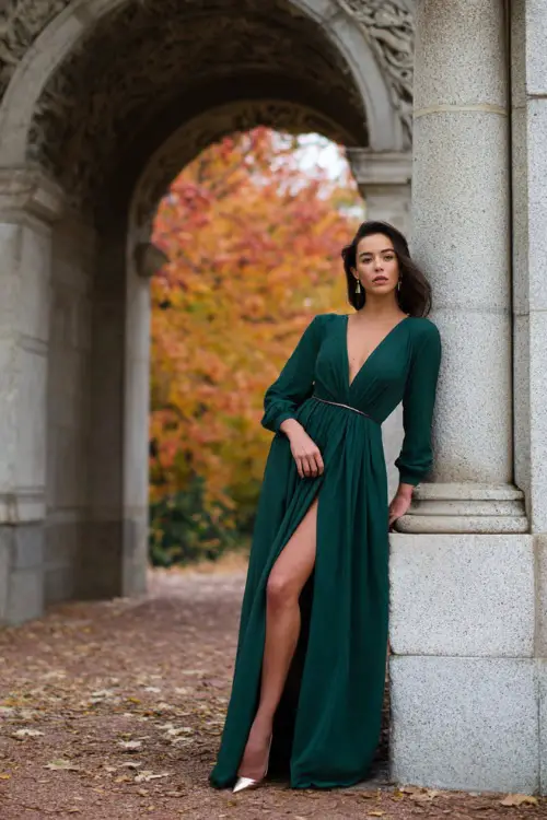 Woman wearing a forest green crepe gown with long sleeves and a V-neckline, paired with delicate stud earrings and a slim metallic belt