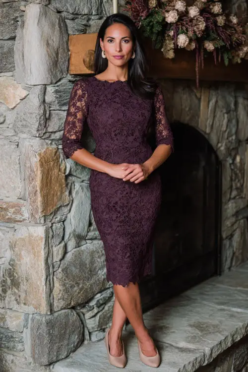 Woman wearing a plum lace sheath dress with scalloped edges and three-quarter sleeves, accessorized with pearl earrings and beige pumps 