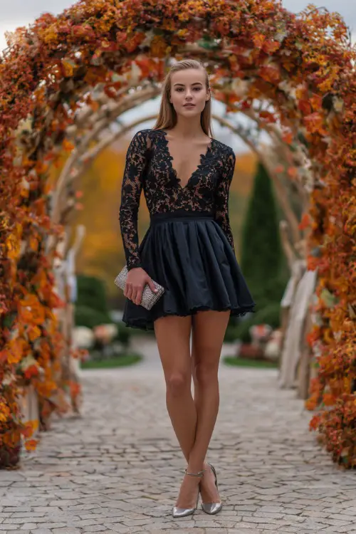 A woman wears a black long-sleeve short dress with lace detailing and a flowy skirt, paired with silver heels and a clutch