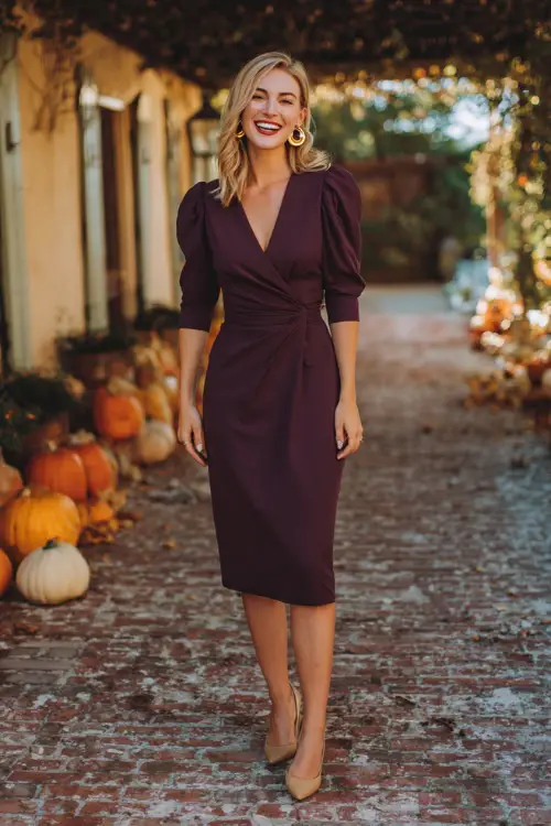 A woman wears a deep plum wrap midi dress with three-quarter sleeves, paired with block heels and gold hoop earrings