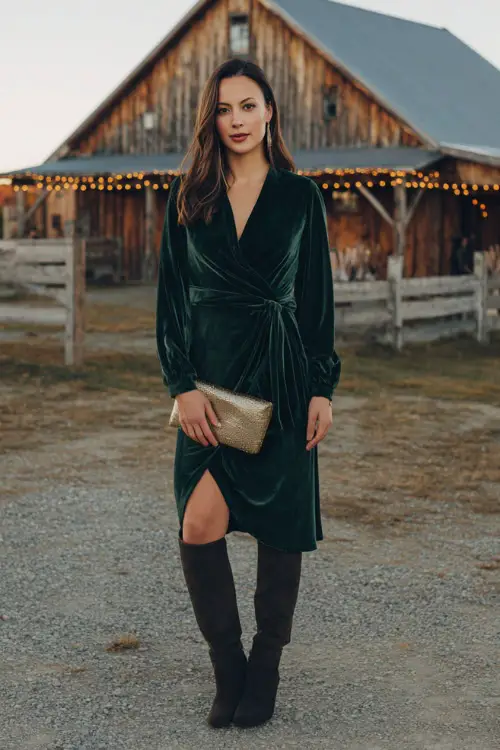 A woman wears a forest green velvet wrap dress with long sleeves and a belted waist, paired with heeled boots and a metallic clutch 