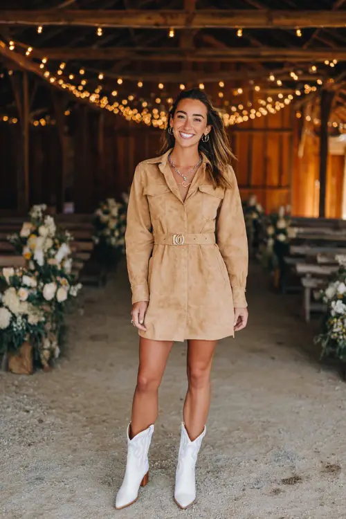 A woman wears a tan suede dress with long sleeves and a fitted waist, styled with white cowboy boots and silver jewelry 