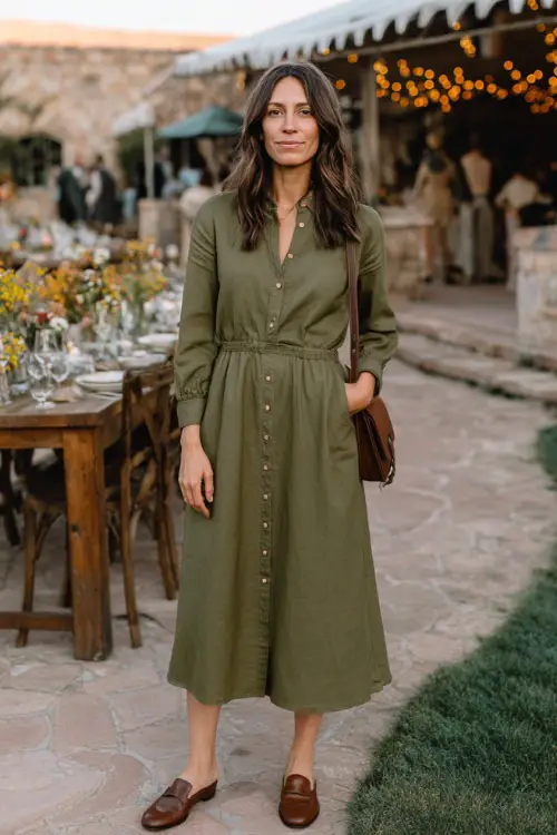A woman wears an olive green cotton midi dress with long sleeves and buttons down the front, paired with loafers and a leather crossbody bag