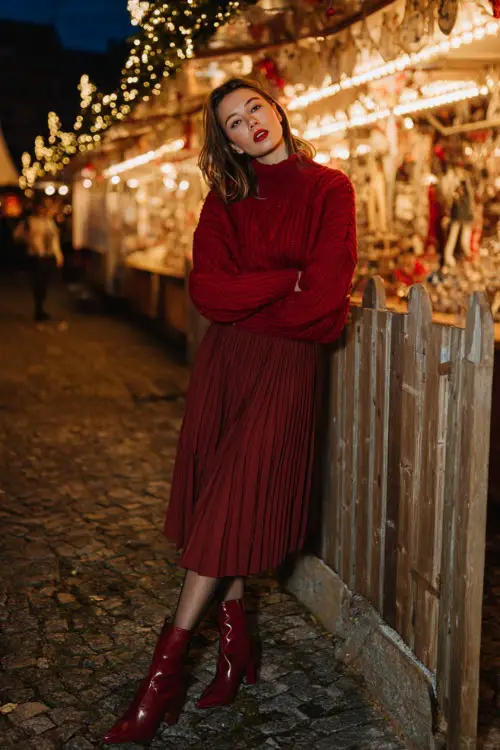 Woman in a festive winter outfit, full-body visible, red knit sweater, pleated midi skirt, sheer tights, heeled boots, posing by a glowing Christmas market display