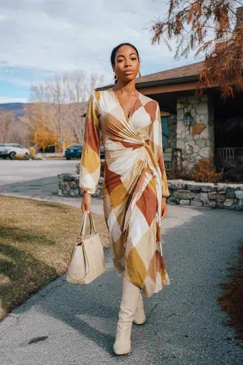 A Black woman dressed in a flowy long-sleeve wrap dress with soft earthy colors, paired with block-heel boots and a structured handbag