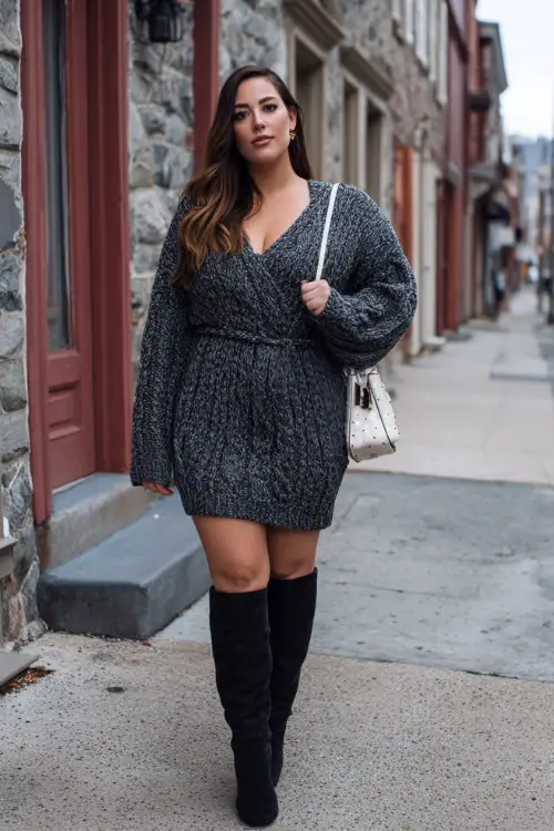 A plus-size woman in a sweater dress with a defined waist, paired with knee-high boots and a structured handbag, posing on a quiet city street during winter brunch hours 