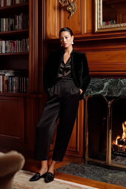 A stylish woman over 30 wears a black velvet jacket layered over a satin blouse and high-waisted trousers