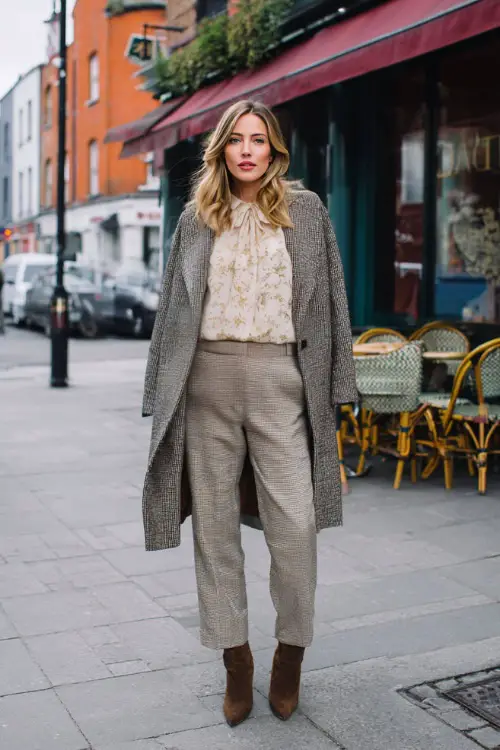 A woman dressed in straight-leg trousers paired with a romantic blouse and a statement wool coat, styled with heeled boots and a small shoulder bag