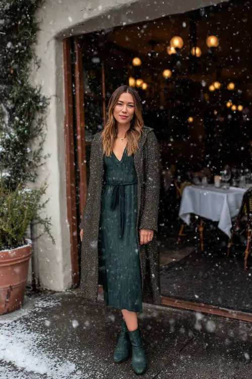 A woman over 30 wears a dark green ribbed midi dress styled with heeled booties and a wool wrap coat