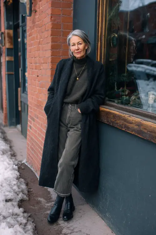 A woman over 50 dressed in straight-leg jeans with a classic knit top and a long wool coat
