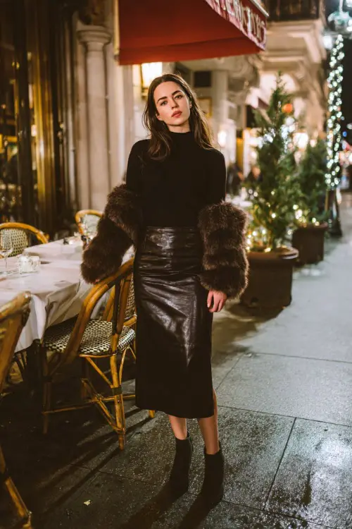 A woman wears a chic black sweater with a leather-look midi skirt, paired with heeled boots and a faux-fur jacket
