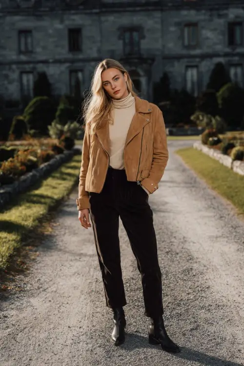 A woman wears a tan suede jacket paired with a cream turtleneck and tailored black pants, styled with leather boots