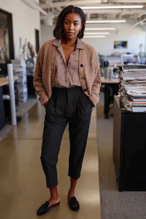 Full-body image of a Black woman wearing a structured cardigan over a button-down shirt, ankle-length tailored pants, and loafers, relaxed yet professional business casual outfit 