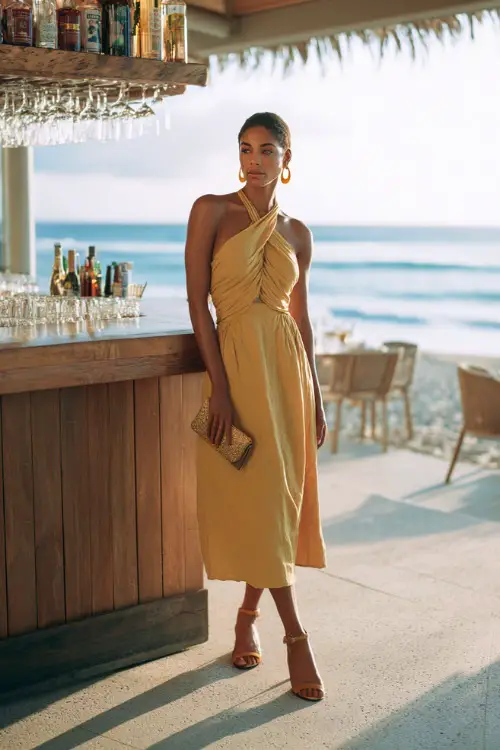A chic woman wearing a breezy midi dress with an open-back design and strappy heels, accessorized with statement earrings and a sleek clutch, standing near a beachside bar with ocean views