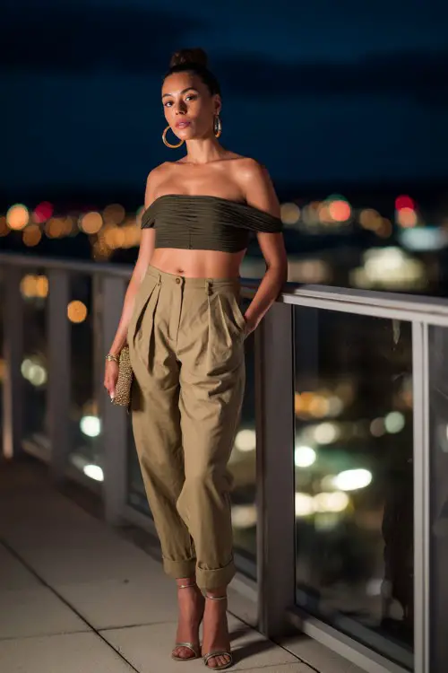 A confident woman wearing high-waisted tailored trousers with a fitted off-shoulder top and sleek heels, accessorized with hoop earrings and a clutch 