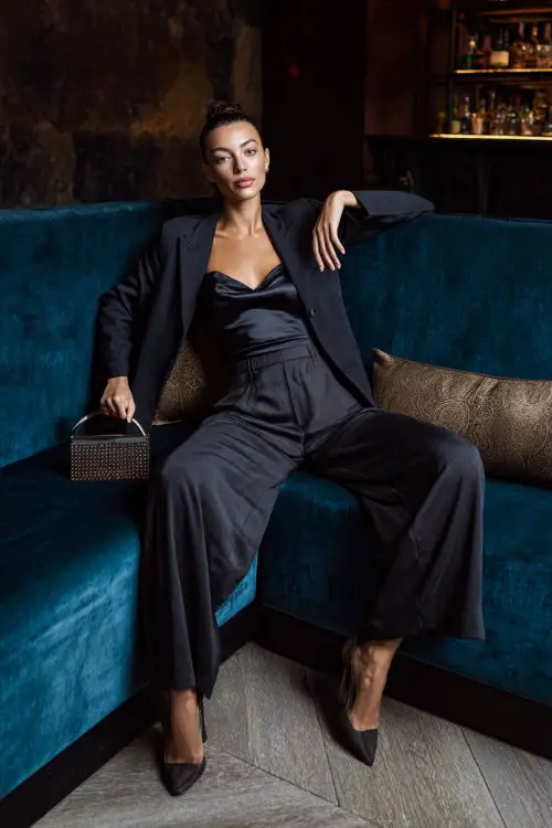 A confident woman wearing tailored wide-leg trousers with a fitted satin top and a sleek blazer, accessorized with a structured handbag and pointed heels 