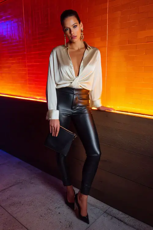 A fashionable woman wearing leather leggings with an oversized blouse slightly tucked in and pointed heels, bold earrings and a sleek clutch (