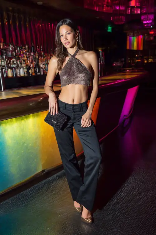 A glamorous woman wearing black high-waisted jeans with a sparkly halter top and strappy metallic heels
