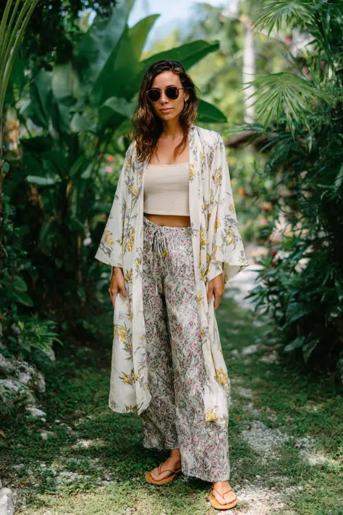 A woman wears a lightweight kimono over a simple tank top and flowy pants, paired with flat sandals and oversized sunglasses