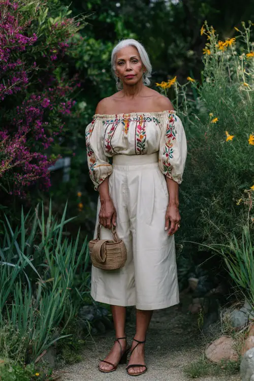 A woman over 50 wears a chic off-shoulder blouse with embroidery paired with a high-waisted midi skirt
