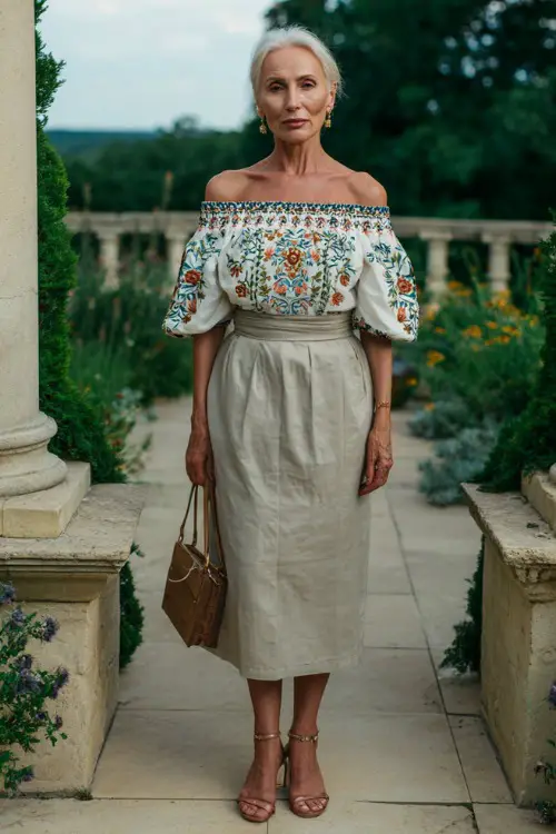 A woman over 60 wears an off-shoulder blouse with embroidery paired with a high-waisted midi skirt