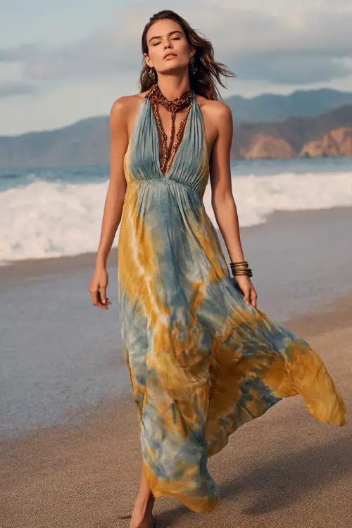 A woman wears a relaxed tie-dye maxi dress with flowing fabric, paired with flat sandals and bold accessories